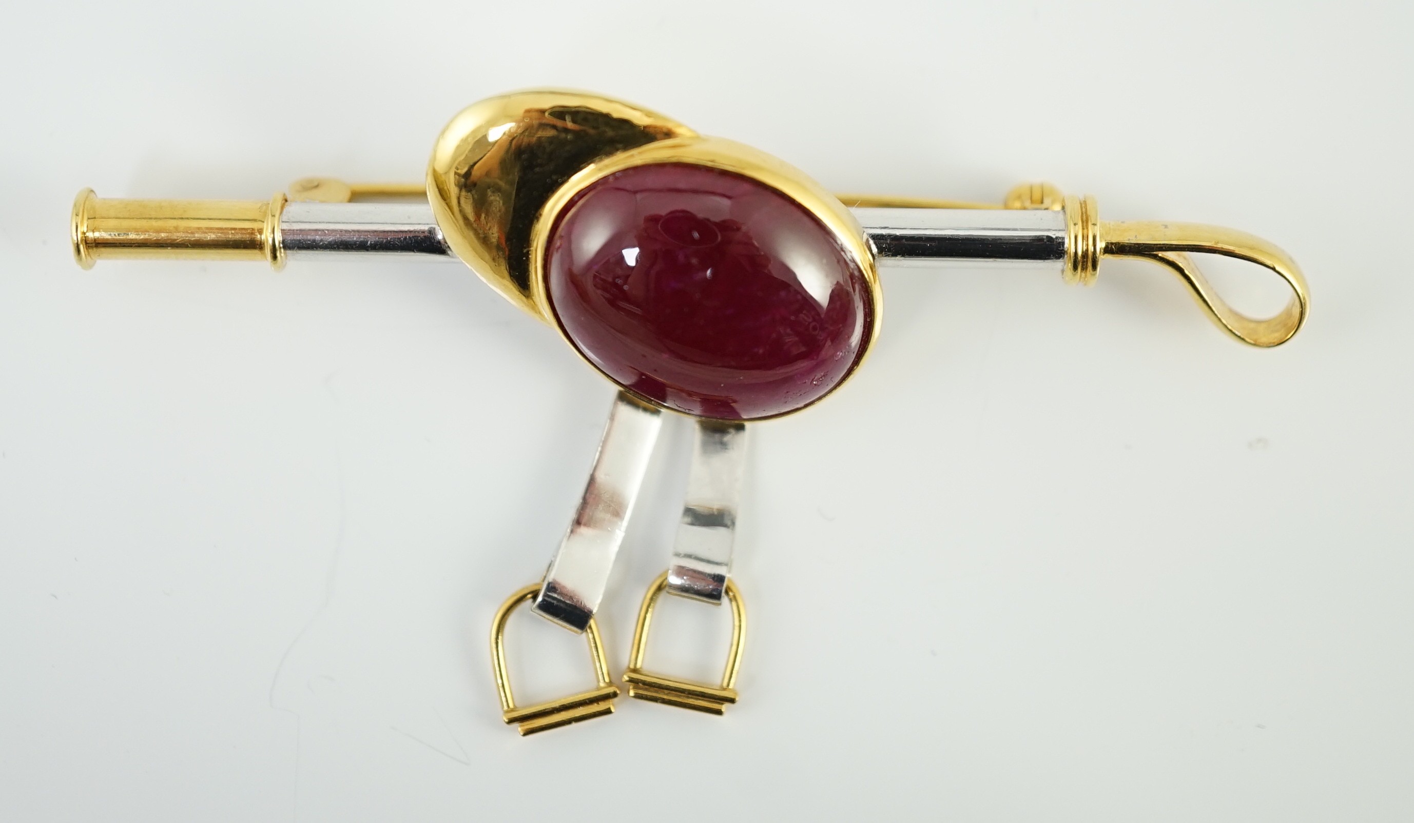 A late 20th century 18ct yellow and white gold, cabochon ruby set ‘jockey cap, riding crop and stirrups’ drop bar brooch